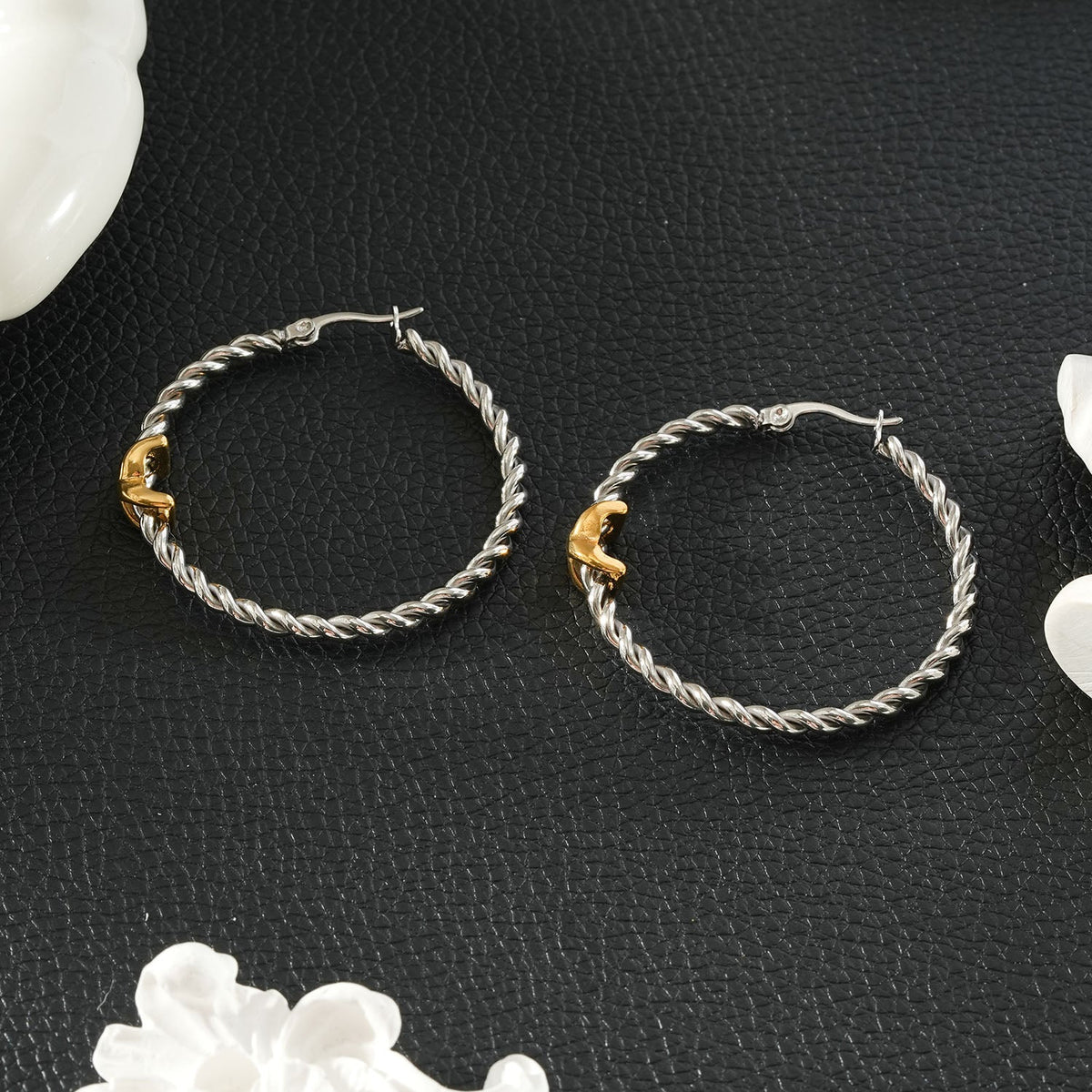 CIPRIANNA silver-tone rope twist hoop earrings with polished gold accents displayed on a textured black background.